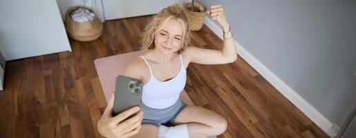 portret van jong sportief vrouw nemen selfie gedurende training opleiding, inhoud Schepper duurt foto's, shows spieren Aan camera, buigen biceps foto