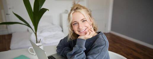 dichtbij omhoog portret van jong glimlachen vrouw model, zit in een kamer met laptop, werken van huis, doet online Cursus, e-learning foto