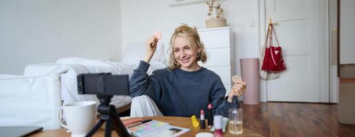 portret van jong vrouw, schoonheid inhoud Schepper, zittend in een kamer in voorkant van digitaal camera, opname bedenken zelfstudie vloggen, tonen kunstmatig gelaats producten foto