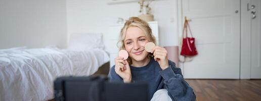 portret van jong vrouw, schoonheid inhoud Schepper, zittend in een kamer in voorkant van digitaal camera, opname bedenken zelfstudie vloggen, tonen kunstmatig gelaats producten foto