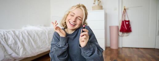 portret van glimlachen mooi vrouw in haar kamer, zittend en tonen lippenstift, aanbevelen favoriete schoonheid Product, inhoud maker opname een van haarzelf voor sociaal media blog foto