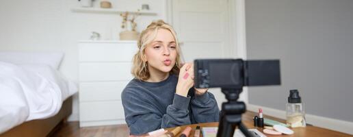 portret van jong creatief sociaal media inhoud Schepper, vrouw tonen lippenstift stalen Aan haar hand, opname over schoonheid en verzinnen, zittend in haar kamer in voorkant van digitaal camera foto