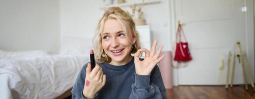 jong vrouw blogger, inhoud Schepper tonen lippenstift en Oke hand- teken, aanbevelen schoonheid Product voor haar publiek Aan sociaal media, opname vlog in kamer foto