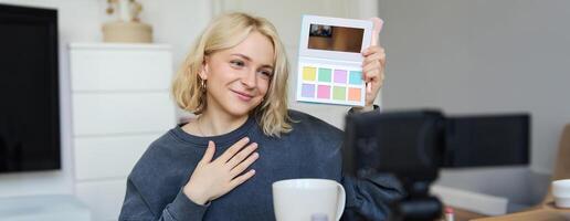 levensstijl blogger, records in haar kamer, heeft een camera Aan koffie tafel, shows oogschaduw palet naar haar volgers, doet bedenken zelfstudie, vlogger werken binnenshuis, creëert inhoud voor sociaal media foto