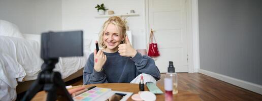 gelukkig jong inhoud Schepper, vrouw tonen lippenstift, opname levensstijl, schoonheid vlog Aan digitaal camera, maakt duimen omhoog hand- gebaar, aanbevelen bedenken Product foto