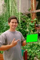 jong Aziatisch Mens richten Bij ipad of tablet met groen scherm in cafe achtergrond foto