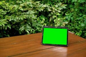 groen scherm ipad of tablet Aan houten tafel met groen planten achtergrond foto