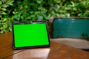 groen scherm ipad of tablet Aan houten tafel met groen planten achtergrond foto