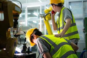 een technicus lijdt een hand- ongeluk terwijl werken met een robot arm in een fabriek met collega's het verstrekken van bijstand foto