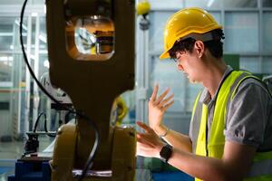 een technicus lijdt een hand- ongeluk terwijl werken met een robot arm in een fabriek met collega's het verstrekken van bijstand foto