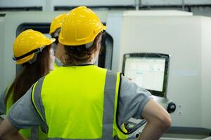 terug visie van groep jong fabriek arbeider vervelend een moeilijk hoed op zoek Bij een computer scherm gebruikt naar controle productie. foto