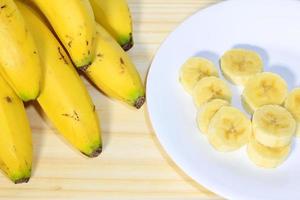 tros bananen op houten tafel naast bord met gesneden fruit foto