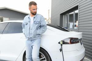 Mens staand door zijn elektrisch auto foto