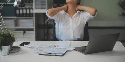 jonge aziatische vrouw die migrainehoofdspanning voelt. vermoeide, overwerkte zakenvrouw financier tijdens het werken op laptopcomputer op kantoor. foto