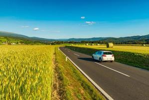 een witte auto rijdt tussen pittoreske velden ergens in oostenrijk foto