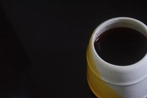 kant visie foto van zwart koffie in een wit en geel kop Aan een zwart keramisch tafel