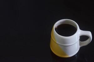 kant visie foto van zwart koffie in een wit en geel kop Aan een zwart keramisch tafel