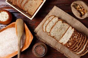 geheel tarwe brood met granen en zaden gesneden Aan houten tafel foto