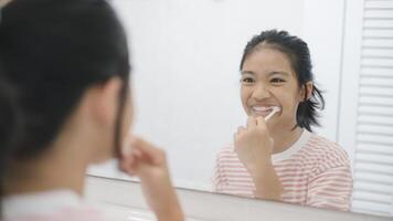 een jong meisje is poetsen haar tanden in voorkant van een spiegel foto