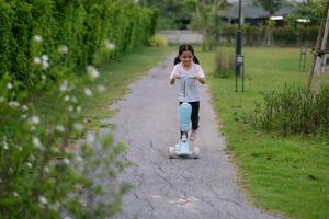 een jong meisje rijden een blauw scooter naar beneden een pad foto