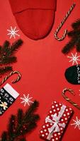 feestelijk Kerstmis kader Aan rood achtergrond Aan nieuw jaar 2024 met tak, geschenk, hoed, snoep karamel, sneeuwvlokken, sokken. top visie, detailopname, plat leggen, kopiëren ruimte, samenstelling, verticaal foto