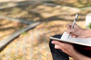 Aziatisch college leerling aan het studeren Aan laptop Bij campus buitenshuis park. Mens schrijven Aan een Notitie boek en werken Aan laptop. leerzaam concept foto