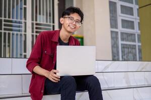 portret van Aziatisch college leerling gebruik makend van laptop op zoek naar camera. een Mens werken met een laptop computer Bij campus foto