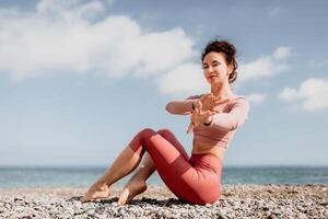 midden- oud goed op zoek vrouw met zwart haar, geschiktheid instructeur in leggings en tops aan het doen uitrekken en pilates Aan yoga mat in de buurt de zee. vrouw geschiktheid yoga routine- concept. gezond levensstijl foto