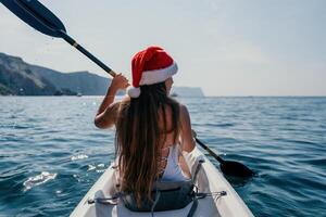 vrouw in kajak terug visie. gelukkig jong vrouw in de kerstman hoed drijvend in kajak Aan kalmte zee. zomer vakantie vakantie en vrolijk vrouw mensen ontspannende hebben pret Aan de boot. foto