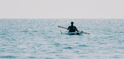 vrouw zee kajak. gelukkig glimlachen vrouw in kajak Aan oceaan, peddelen met houten roeispaan. kalmte zee water en horizon in achtergrond. actief levensstijl Bij zee. zomer vakantie. foto