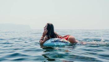 vrouw zomer zee. gelukkig vrouw zwemmen met opblaasbaar donut Aan de strand in zomer zonnig dag, omringd door vulkanisch bergen. zomer vakantie concept. foto