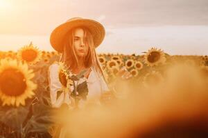 vrouw in zonnebloem veld. gelukkig meisje in een rietje hoed poseren in een enorm veld- van zonnebloemen Bij zonsondergang, genieten nemen afbeelding buitenshuis voor herinneringen. zomer tijd. foto