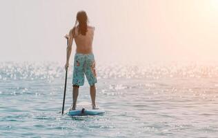 Mens sup zee. sterk atletisch Mens leert naar peddelen sup staand Aan bord in Open zee oceaan Aan zonnig dag. zomer vakantie vakantie en reizen concept. antenne visie. langzaam beweging foto