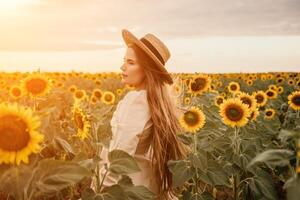vrouw in zonnebloem veld. gelukkig meisje in een rietje hoed poseren in een enorm veld- van zonnebloemen Bij zonsondergang, genieten nemen afbeelding buitenshuis voor herinneringen. zomer tijd. foto