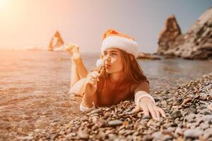 vrouw reizen zee. gelukkig toerist genieten nemen afbeelding Aan de strand voor herinneringen. vrouw reiziger in de kerstman hoed looks Bij camera Aan de zee baai, sharing reizen avontuur reis foto