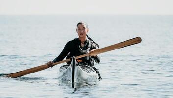 vrouw zee kajak. gelukkig glimlachen vrouw in kajak Aan oceaan, peddelen met houten roeispaan. kalmte zee water en horizon in achtergrond. actief levensstijl Bij zee. zomer vakantie. foto