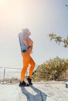 geschiktheid vrouw zee. gelukkig midden- oud vrouw in oranje sportkleding opdrachten ochtend- buitenshuis Aan yoga mat met laptop in park over- oceaan strand. vrouw geschiktheid pilates yoga routine. gezond levensstijl. foto