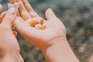 vrouw aan het eten melkachtig amandel noten. een jong Kaukasisch vrouw hakken vers groen amandel na ochtend- geschiktheid yoga in de buurt zee. enkel en alleen handen zijn zichtbaar. gezond veganistisch voedsel. langzaam beweging. dichtbij omhoog foto