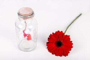liefde bericht in een fles. rollen van wit papier met rood draad en rood gerbera bloem Aan een wit achtergrond. heilige valentijnsdag dag concept foto