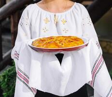 traditioneel eigengemaakt spons taart gehouden door vrouw in volk kostuum foto