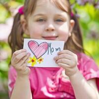 weinig meisje geven haar hand- schrijven groet kaart naar haar mama. foto