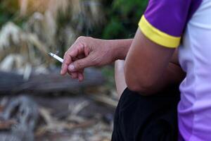 Aziatisch man's hand- houdt een lit sigaret en zit alleen roken in de roken hoek van zijn huis. foto