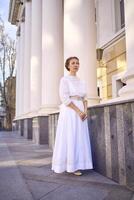 elegant midden- leeftijd vrouw in wit wijnoogst jurk in de buurt theater met antiek zuilengalerijen foto