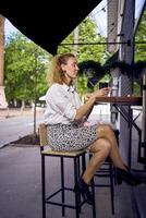 een mooi midden- leeftijd vrouw in jaren 70, 80s stijl kleren drankjes koffie zittend Bij de bar in een modern cafe foto