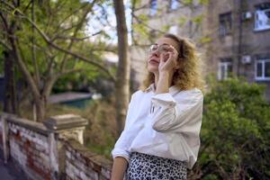 midden- leeftijd vrouw in jaren 70, 80s stijl kleren met een koffie bekladden Aan haar blouse in voorkant van grijs huizen van de jaren 70 foto