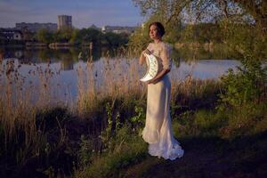 een vrouw in een wit wijnoogst jurk Aan de kust van een meer Bij zonsondergang houdt een maan vormig spiegel foto