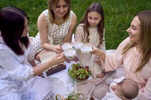 twee Dames en hun kinderen hebben een picknick Aan de gazon foto