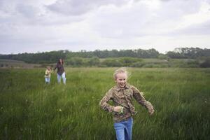 twee weinig zussen en moeder rennen en lancering een vlieger in een veld- foto
