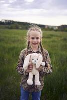 een mooi blond meisje met haar speelgoed- konijn is spelen in de veld- foto