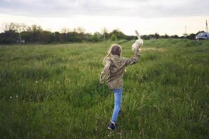 een mooi blond meisje met haar speelgoed- konijn is spelen in de veld- foto